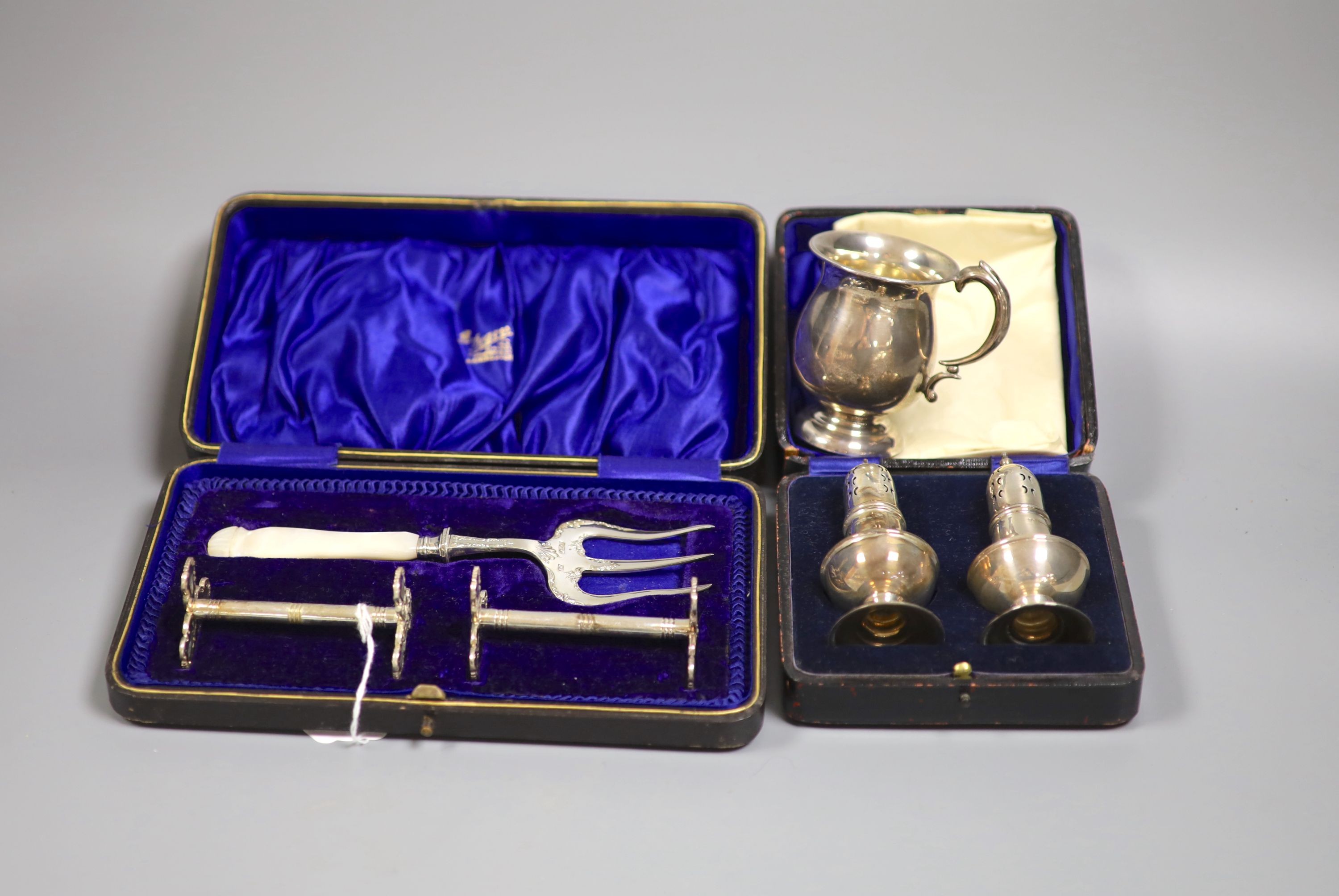 A 1920's silver small mug, a cased pair of silver pepperettes and a cased pair of knife rests and fork.